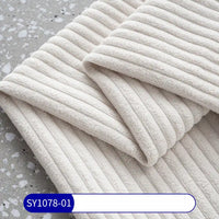 A folded piece of Longan Craft’s 2.5 Wale Corduroy Fabric By The Yard in cream lies on a gray terrazzo surface, showing off its soft, ribbed texture. A blue and white label at the bottom reads SY1078-01.
