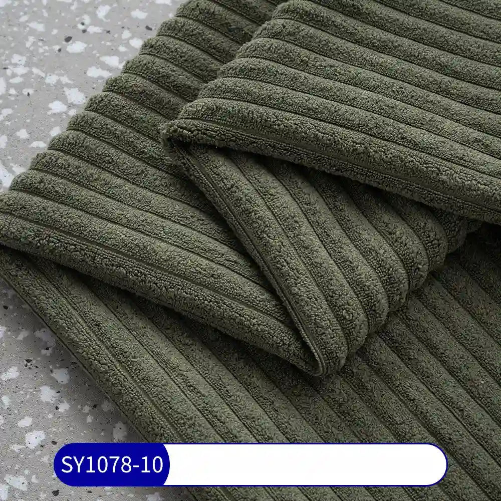 A close-up of dark green, ribbed 2.5 Wale Corduroy Fabric By The Yard from Longan Craft, neatly folded on gray terrazzo. The texture resembles premium corduroy. A label at the bottom left shows SY1078-10 on a blue background.