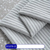 A close-up of light gray, ribbed towels on a speckled surface resembles the texture of Longan Craft’s 2.5 Wale Multicolor Polyester Corduroy Fabric by the yard, as highlighted by the label SY1078-15.