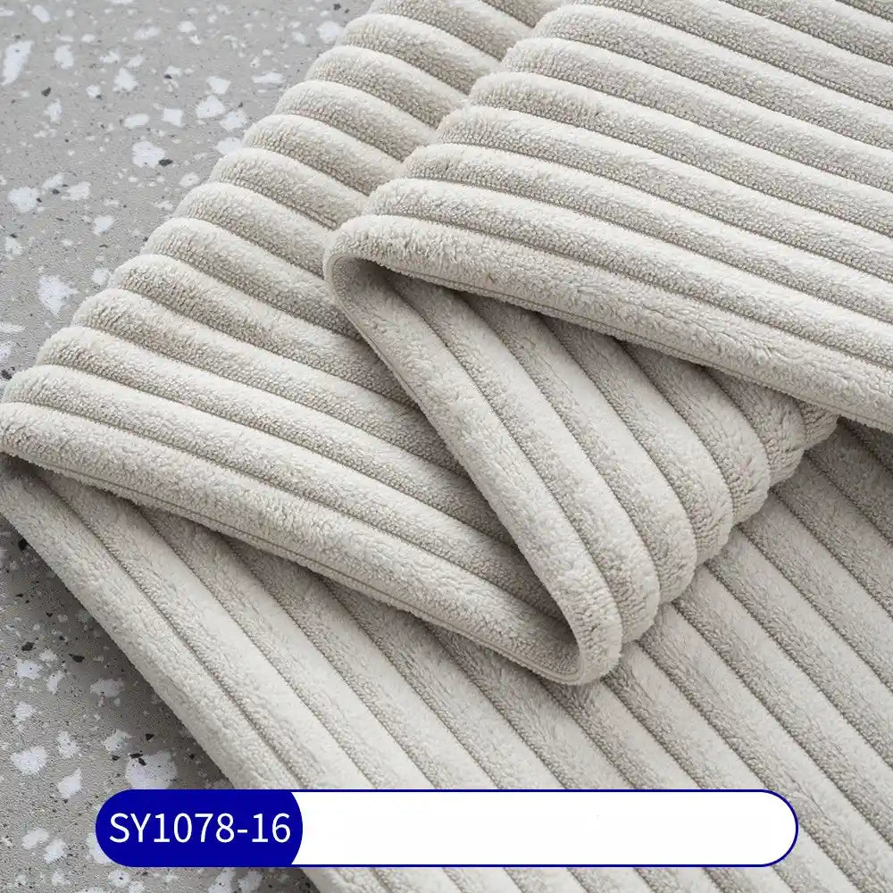 A close-up of soft, light grey 2.5 Wale Corduroy Fabric by Longan Craft is shown folded on a speckled surface, highlighting its plush ribbed texture. The label reads SY1078-16. Suitable for upholstery and crafts, sold by the yard.