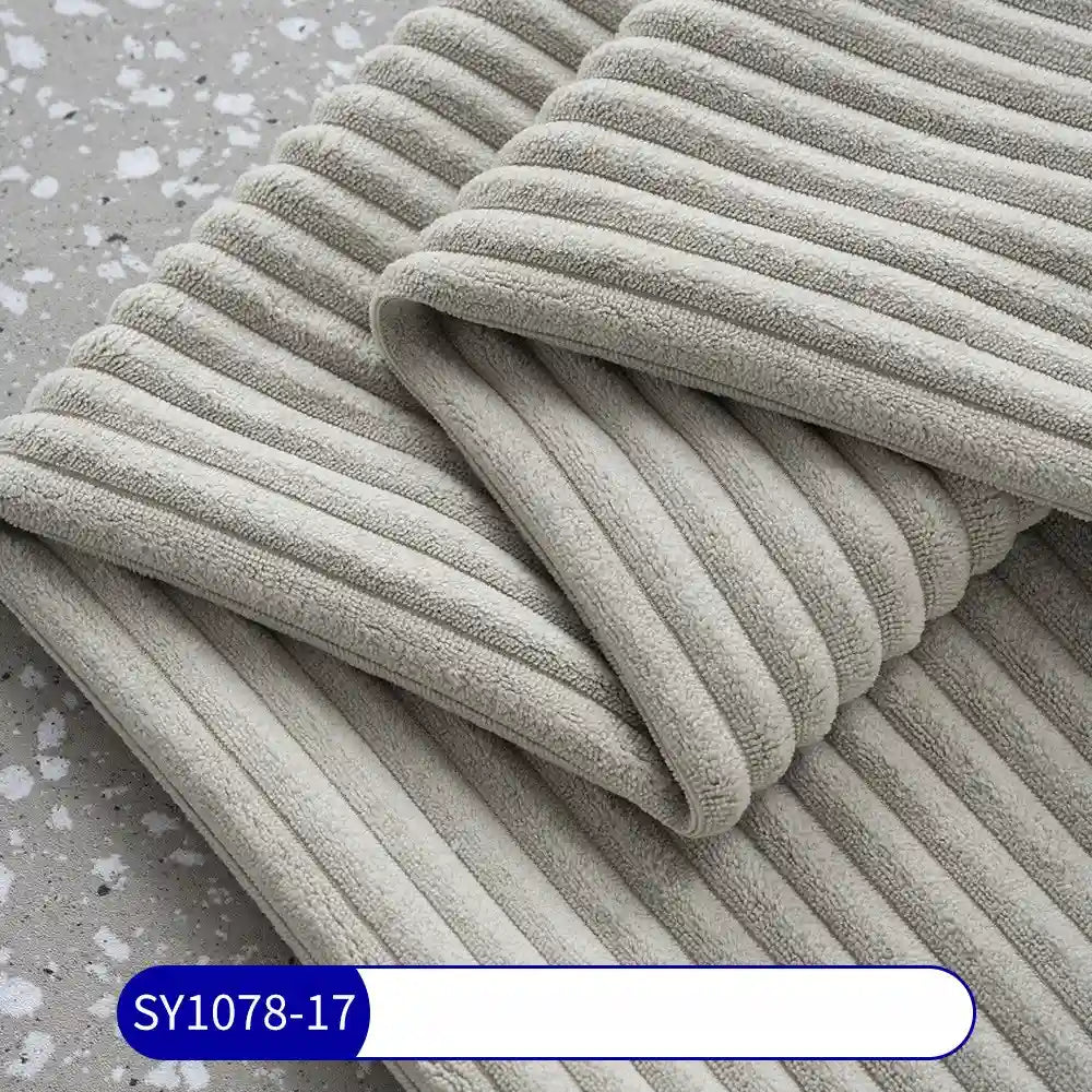 A close-up shows a folded light gray 2.5 Wale Corduroy Fabric by Longan Craft on a gray speckled surface, highlighting its corduroy texture. A label at the bottom reads SY1078-17 in white on blue.