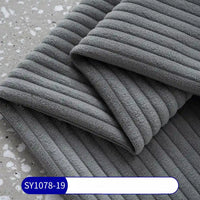 A close-up of folded 2.5 wale corduroy fabric by the yard from Longan Craft, in gray polyester, on a speckled surface. A blue and white label at the bottom reads SY1078-19.