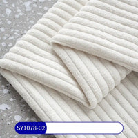 A folded 2.5 Wale Corduroy Fabric by Longan Craft in off-white lies on a speckled grey surface, with a blue and white label at the bottom left corner displaying code SY1078-02.