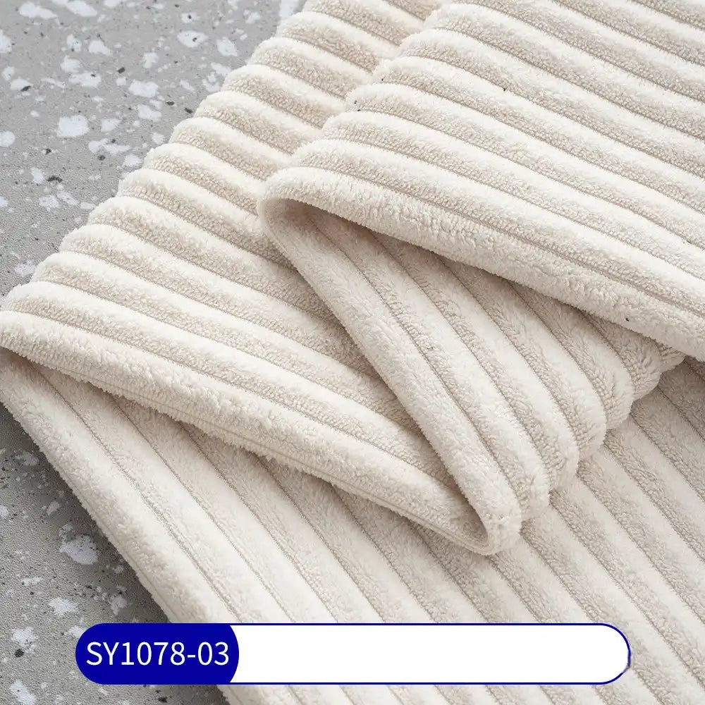 A close-up of a folded, cream-colored 2.5 Wale Corduroy Fabric by Longan Craft shows its soft, corduroy-like texture on a speckled gray surface. A blue and white SY1078-03 label is visible at the bottom left.
