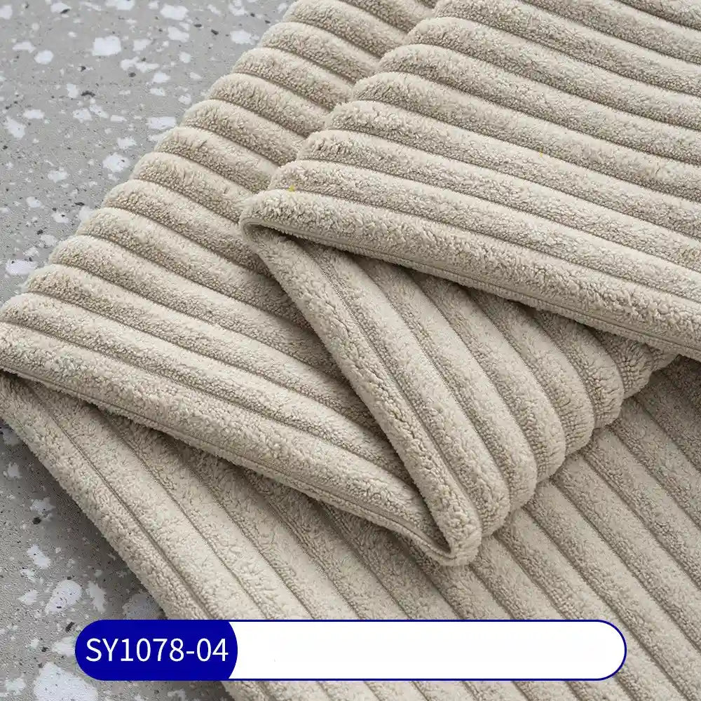Folded beige towels, evoking 2.5 wale corduroy, rest on a grey speckled surface. The Longan Craft 2.5 Wale Corduroy Fabric By The Yard (SY1078-04) is labeled in blue and white at the bottom of the image.