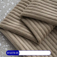 A close-up of folded, ribbed beige towels on a speckled gray surface highlights the rich texture of Longan Craft’s 2.5 Wale Corduroy Fabric By The Yard, Multicolor Polyester Upholstery Material. A label at the bottom reads SY1078-05 on blue and white.