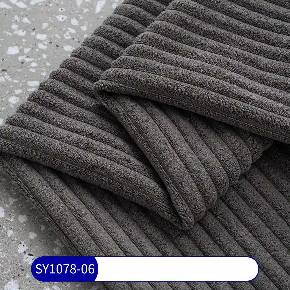 A close-up of folded dark gray 2.5 wale corduroy fabric by the yard from Longan Craft, featuring a textured, striped pattern like classic corduroy and a SY1078-06 label, displayed on a speckled gray surface.