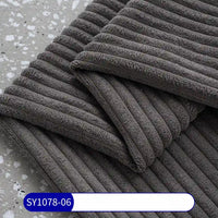 A close-up of folded dark gray 2.5 wale corduroy fabric by the yard from Longan Craft, featuring a textured, striped pattern like classic corduroy and a SY1078-06 label, displayed on a speckled gray surface.