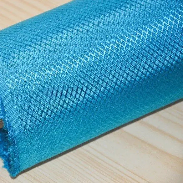 A close-up of Longan Craft’s 210D Honeycomb Pattern Oxford Fabric by the yard, a colorful PU coated, waterproof material for outdoor use, shown in blue with a grid pattern on a light wooden surface.