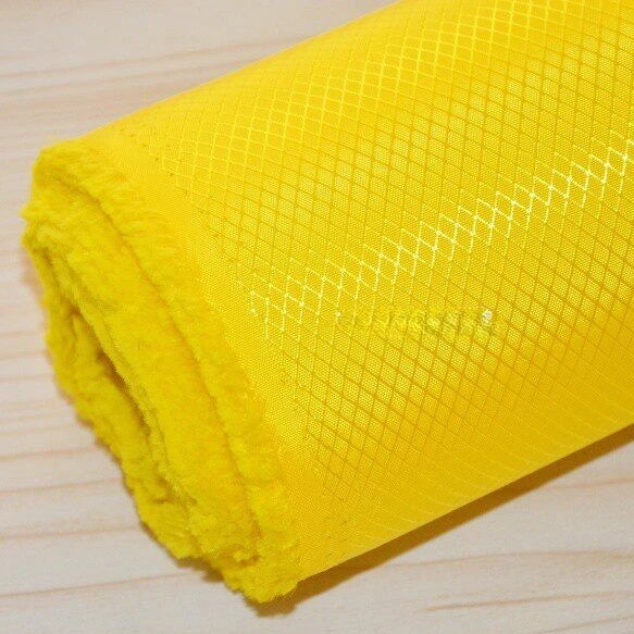 A close-up of Longan Craft's 210D Honeycomb Pattern Oxford Fabric by the yard shows its vibrant yellow, PU-coated, waterproof surface with a diamond texture on top and soft edges, displayed on a light wooden background.