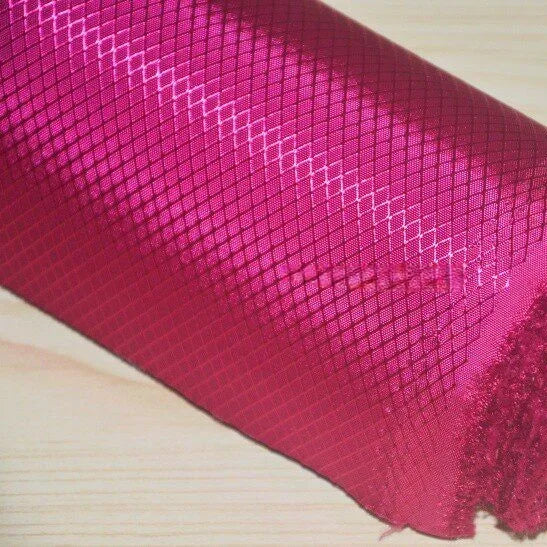 A roll of Longan Craft 210D Honeycomb Pattern Oxford Fabric By The Yard, a colorful PU-coated, waterproof material with a subtle diamond design, sits on a light wooden surface—ideal for outdoor use and gear.