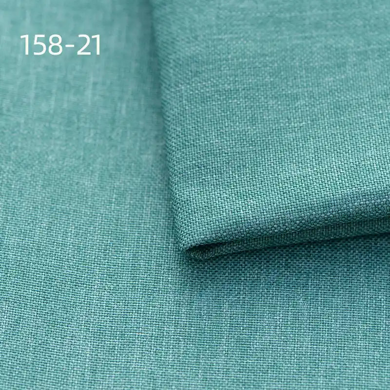 A close-up of Longan Craft Faux Linen Upholstery Fabric in teal shows its smooth, textured polyester surface. One piece is folded over another, with “158-21” printed in white at the upper left. Ideal for reupholstering chairs, sofas, or curtains.