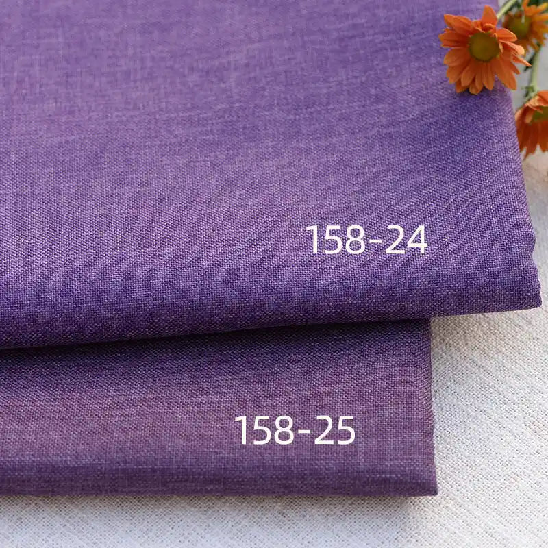 Two folded pieces of Longan Craft Faux Linen Upholstery Fabric, labeled 158-24 and 158-25, are stacked on a light surface with orange flowers in the upper right corner. The polyester fabric is ideal for upholstering furniture.