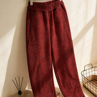 A pair of red high-waisted tailored pants made using the Structured Pants Sewing Pattern by Longan Craft hangs on a hanger in a sunlit room, beside a wire basket and reed diffuser. Free PDF pattern download available.