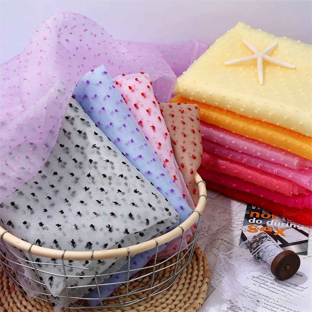 Folded stacks of Sheer Swiss Dot Organza Fabric By The Yard with colorful 3D dots resting in a wire basket and topped with a decorative starfish.