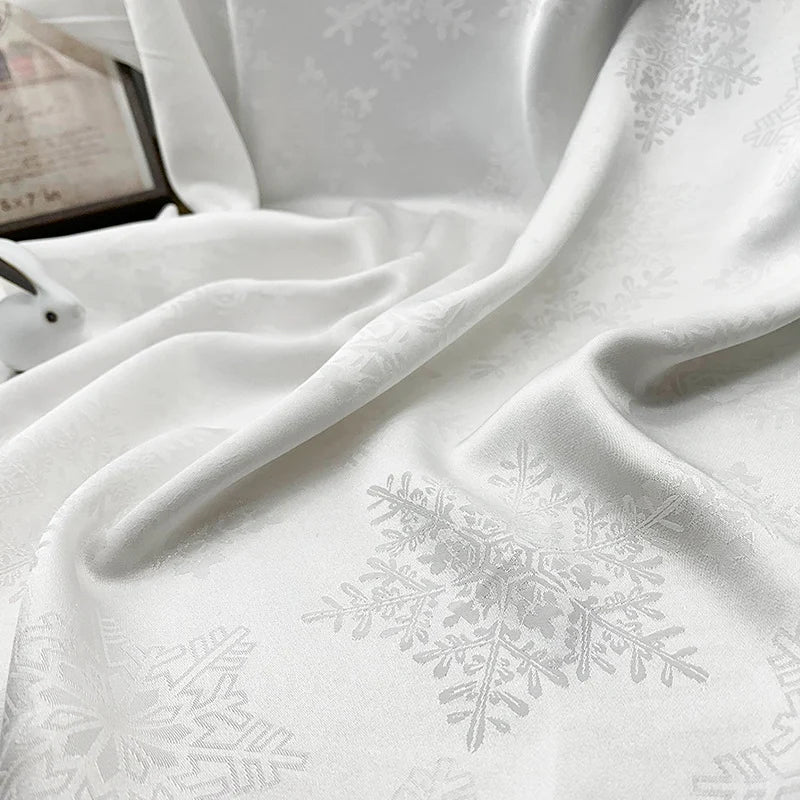 A close-up of Longan Craft’s Snowflake Jacquard Satin Fabric By The Yard in white, featuring a subtle snowflake pattern woven into smooth polyester satin, draped in soft folds—perfect for dresses and crafts.