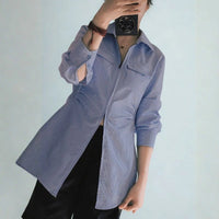 A person wears a light blue shirt made from the Longan Craft Women’s Zip-Front Shirt Sewing Pattern (PDF), paired with black shorts, in a mirror selfie. Their face is hidden by their phone; one sleeve is slightly rolled up against a plain background.