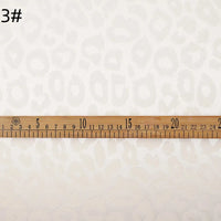 A close-up of Longan Craft Leopard Jacquard Satin Fabric By The Yard, featuring a subtle leopard print in white, a wooden ruler in centimeters across the soft polyester satin, and "3#" text in the top left corner.