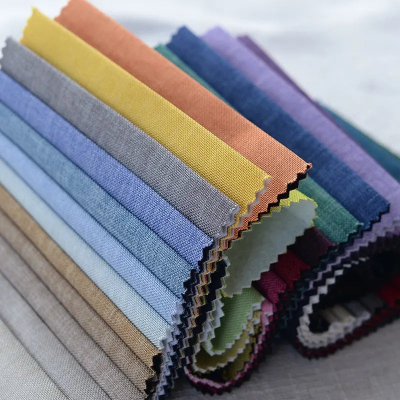 A stack of Longan Craft Faux Linen Upholstery Fabric by the yard in blue, yellow, orange, green, and beige is neatly arranged in an overlapping row with pinked edges for reupholstering chairs, sofas, or curtains.