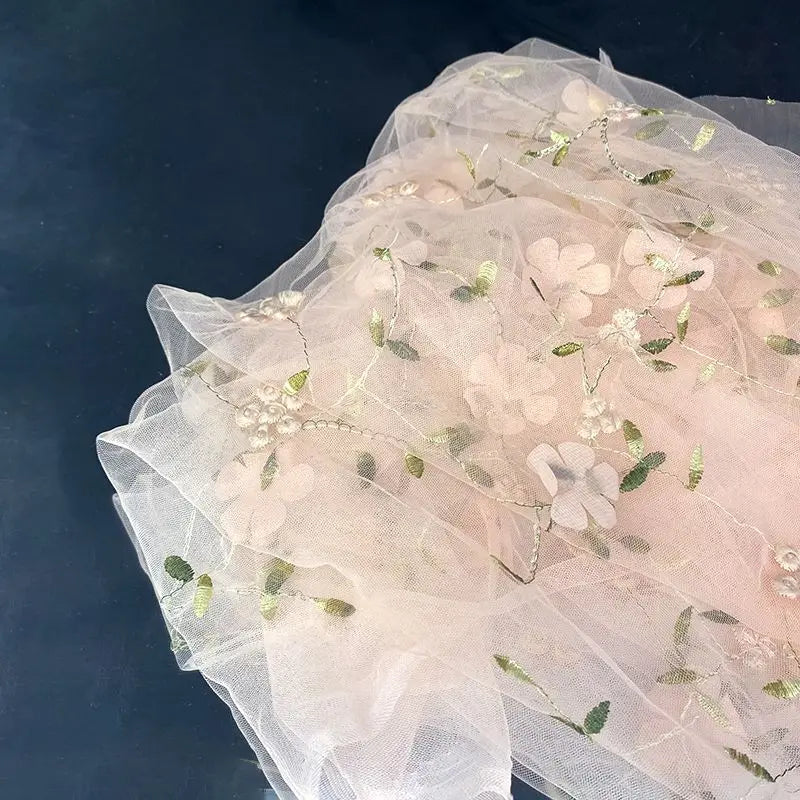 A close-up of Longan Craft’s 3D Floral Embroidered Tulle Fabric by the Yard, a colorful botanical bridal tulle material with embroidered flowers and leaves displayed on a dark surface.