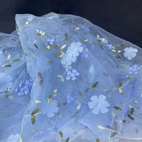 Longan Craft’s 3D Floral Embroidered Tulle Fabric by the yard features colorful botanical embroidery with white flowers, blue blooms, and gold leaves—ideal for bridal gowns, as shown against a dark background.