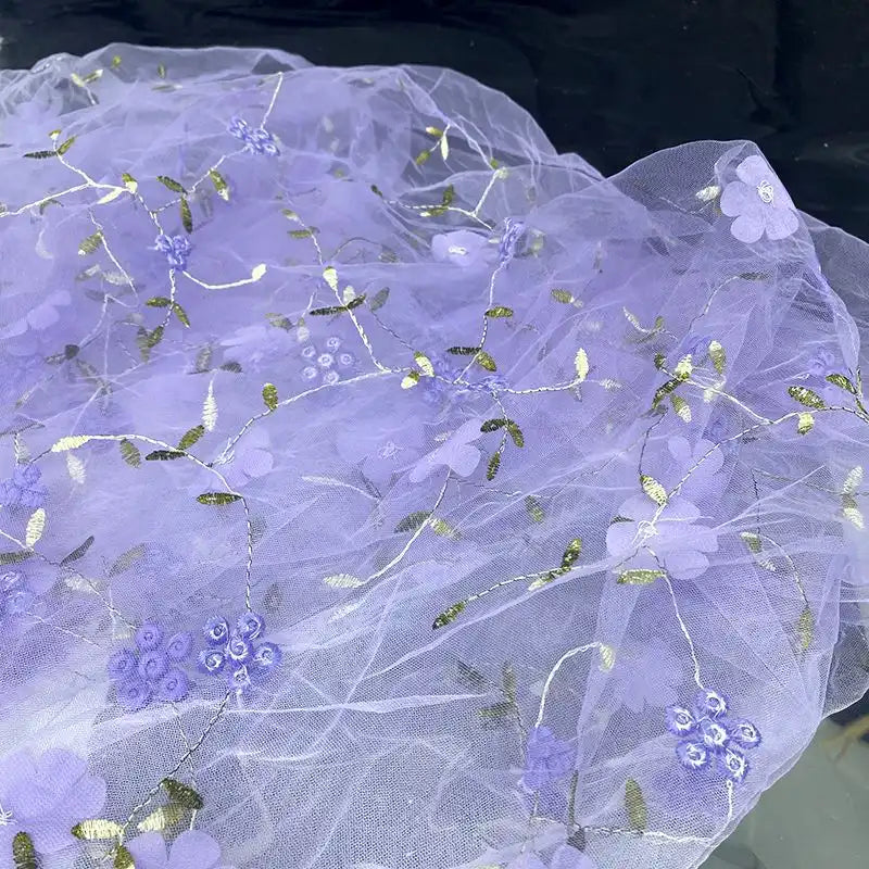Longan Craft's 3D Floral Embroidered Tulle Fabric by the yard features colorful botanical embroidery—delicate purple flowers, green leaves, and gold accents—making it perfect bridal tulle material for romantic wedding dresses.
