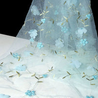 Longan Craft's 3D Floral Embroidered Tulle Fabric By The Yard showcases colorful botanical embroidery with delicate flowers, green leaves, and stems—ideal Bridal Tulle Material for wedding dresses. Draped over white against black for elegant contrast.