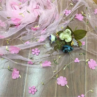 Longan Craft’s 3D Floral Embroidered Tulle Fabric by the yard features colorful botanical embroidery, ideal for bridal gowns or wedding dresses, and is displayed on a wooden surface.