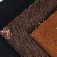 Three folded pieces of Longan Craft 3D Patterned Embroidery Corduroy Fabric by the Yard in black, brown, and rust, each with small blue and orange geometric embroidery—perfect fine wale cotton corduroy for jackets and clothing.