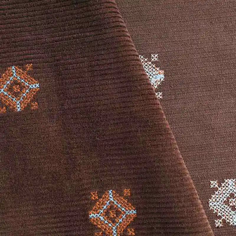 Close-up of Longan Craft 3D Patterned Embroidery Corduroy Fabric by the yard, featuring blue, orange, and white diamond embroidery on premium cotton fine wale corduroy. Folds highlight the detailed stitching and comfy texture.