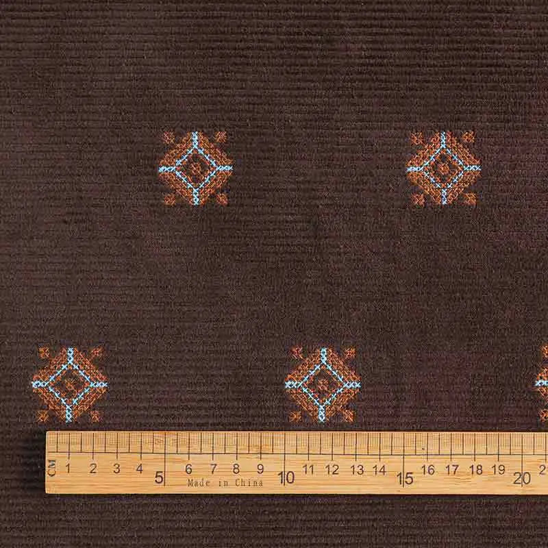 A wooden ruler rests on Longan Craft’s 3D Patterned Embroidery Corduroy Fabric—a comfy, fine wale cotton corduroy textile with blue and orange motifs, ideal for jackets or detailed clothing projects.