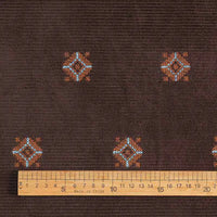 A wooden ruler rests on Longan Craft’s 3D Patterned Embroidery Corduroy Fabric—a comfy, fine wale cotton corduroy textile with blue and orange motifs, ideal for jackets or detailed clothing projects.