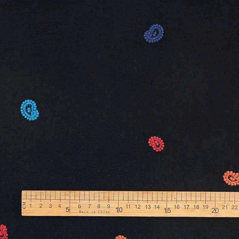 A wooden ruler lies on Longan Craft’s 3D Patterned Embroidery Corduroy Fabric, a fine wale cotton by the yard with small red, orange, and blue paisley embroidery—ideal for jackets. The ruler displays centimeter measurements.