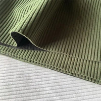 Close-up of Longan Craft 4.5 Wale Polyester Corduroy Fabric in green, folded with visible edge stitching, resting on white ribbed fabric; this solid wide wale corduroy is ideal for pants and available by the yard.