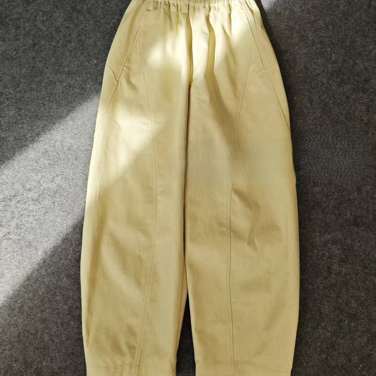 A pair of loose-fitting, high-waisted, light yellow pants with an elastic waistband, displayed on a gray surface—perfect to sew using the Longan Craft Structured Pants Sewing Pattern | Free PDF Pattern Download.