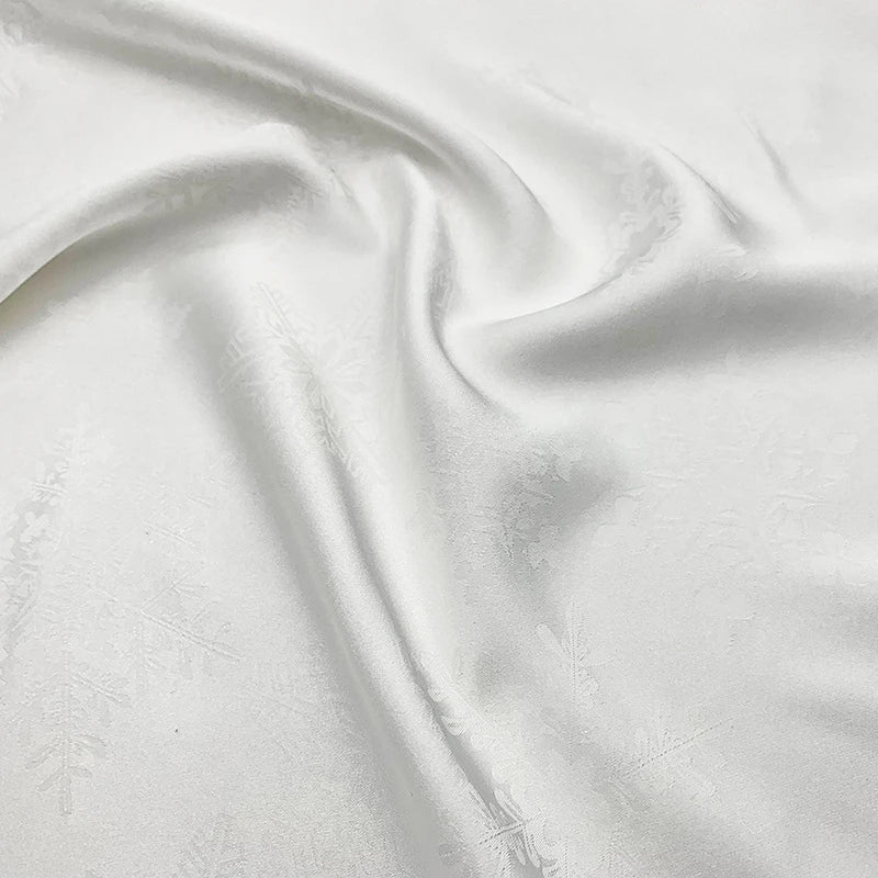 A close-up of smooth, white Longan Craft Snowflake Jacquard Satin Fabric by the yard—polyester satin with a subtle snowflake pattern, softly draped to show light folds and a gentle sheen, ideal for elegant dresses.