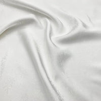 A close-up of smooth, white Longan Craft Snowflake Jacquard Satin Fabric by the yard—polyester satin with a subtle snowflake pattern, softly draped to show light folds and a gentle sheen, ideal for elegant dresses.