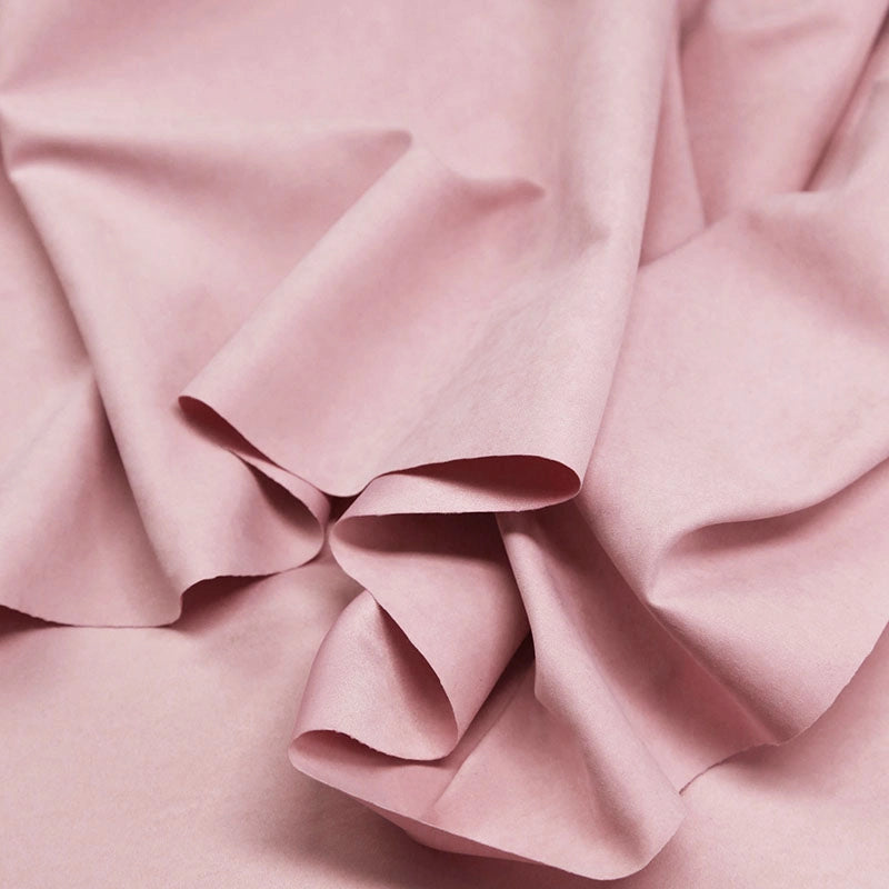 A close-up of Longan Craft's Multi Color Microsuede Polyester Peachskin Fabric By The Yard shows its soft, light pink, brushed peach skin texture with gentle folds and creases—perfect for cozy clothing.