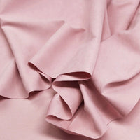 A close-up of Longan Craft's Multi Color Microsuede Polyester Peachskin Fabric By The Yard shows its soft, light pink, brushed peach skin texture with gentle folds and creases—perfect for cozy clothing.