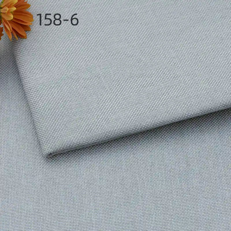 A close-up of Longan Craft’s Faux Linen Upholstery Fabric By The Yard shows two overlapping pieces in light gray with a woven texture. An orange flower appears at the top left, along with the code 158-6.