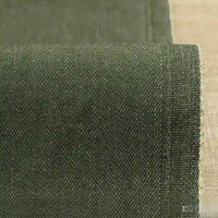 A close-up of Longan Craft’s 9.5oz Stretch Denim Fabric By The Yard shows its dark green, medium-weight cotton material with a subtle diagonal weave and neatly finished selvage on a light wood surface—perfect for jeans and denim projects.