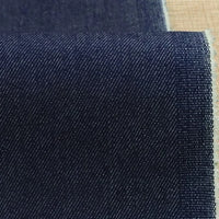 A close-up of Longan Craft's 9.5oz Stretch Denim Fabric By The Yard in solid dark blue cotton, showing diagonal weaving patterns and a slightly frayed edge, displayed on a light beige surface—ideal material for jeans or crafts.