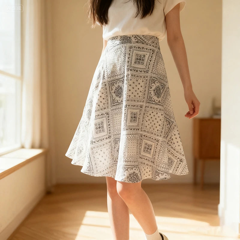 A woman stands indoors in sunlight beside a window, wearing a white top and a knee-length skirt made from the Longan Craft Women A-line Midi Skirt Sewing Pattern—available as a free PDF skirt pattern with gray geometric and floral designs.
