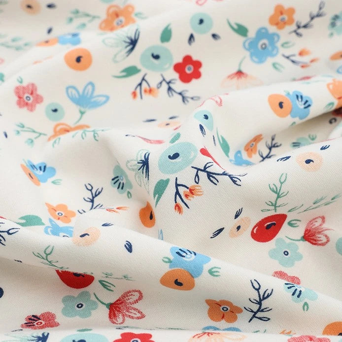 Longan Craft's Animal and Botanical Printed Jersey Fabric by the yard is a heavy weight, cream-colored cotton jersey with a whimsical floral and animal pattern in red, blue, orange, and green. The soft sweatshirt fabric has a slightly wrinkled texture.