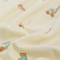 A close-up of Longan Craft's Animal and Botanical Printed Jersey Fabric by the yard, a heavy weight 100% cotton sweatshirt jersey featuring playful rain boot, rainbow, and watering can illustrations in pastel on cream. Soft fabric is slightly draped.