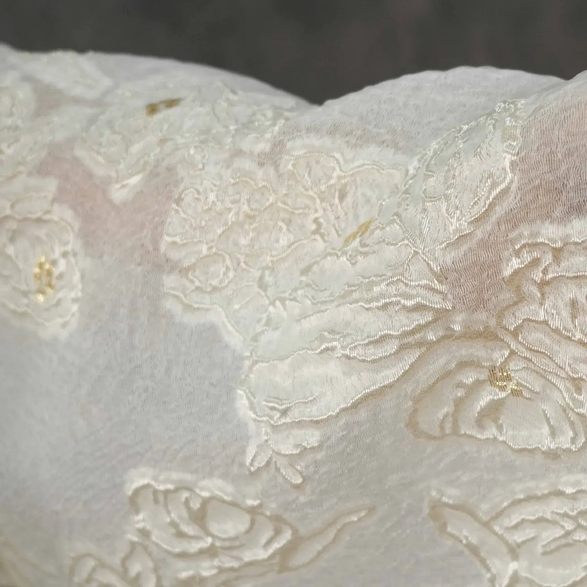 Close-up of Apricot Rose Embossed Organza Fabric by Longan Craft features 3D floral jacquard with lustrous embroidery, creating a textured and elegant look—ideal soft organza for summer dresses. Background is blurred to highlight the intricate design.