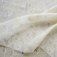 The Apricot Rose Embossed Organza Fabric by Longan Craft, featuring 3D floral jacquard and soft organza with gold accents, is draped over a surface with newspaper print.
