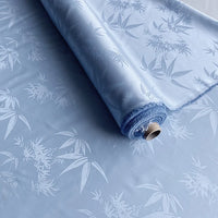 A partially unrolled roll of Longan Craft Bamboo Jacquard Mulberry Silk Fabric in light blue, featuring a subtle, glossy floral pattern—ideal colorful rayon silk for cozy lining projects.