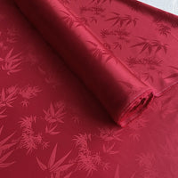 A roll of Bamboo Jacquard Mulberry Silk Fabric by Longan Craft, featuring a subtle, glossy pattern in vibrant rayon silk, is partially unrolled on a flat surface.
