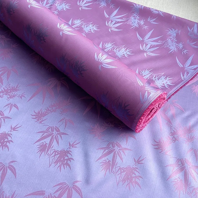 A roll of Bamboo Jacquard Mulberry Silk Fabric by Longan Craft in purple shades, featuring a subtle jacquard pattern, is partially unrolled on a flat surface. This colorful rayon silk fabric is ideal for cozy linings.
